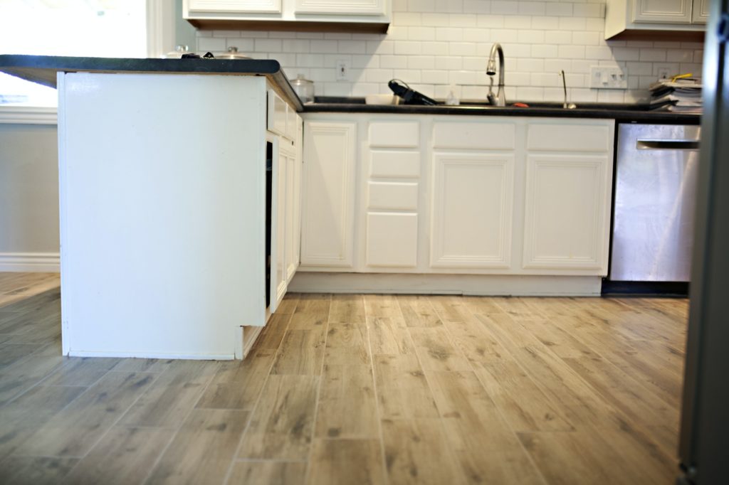 Home with white kitchen cabinets and wood tile floor